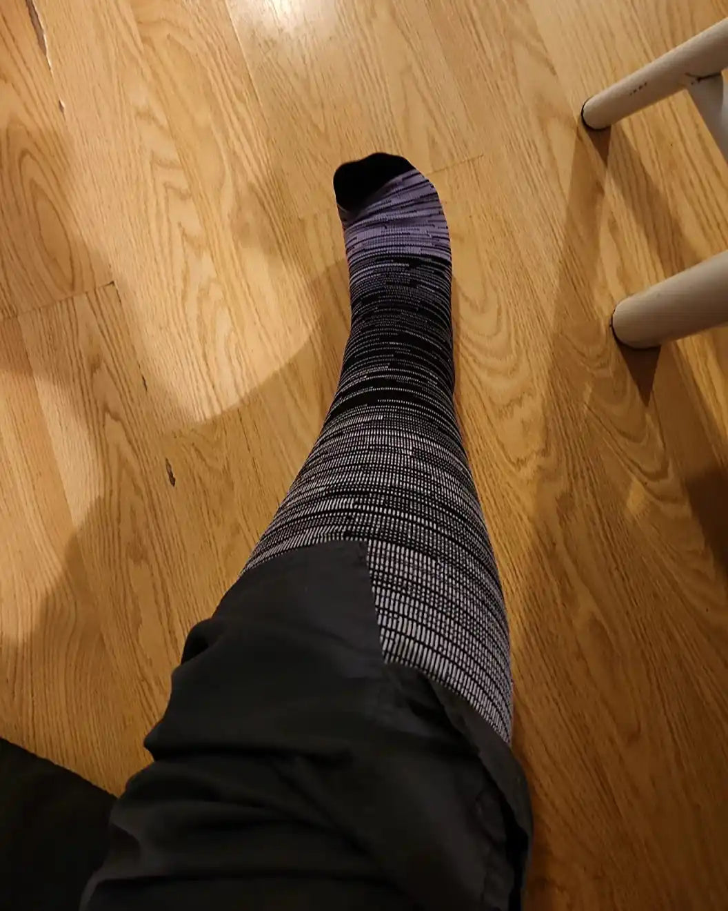 La jambe d'une personne portant une chaussette de compression à motifs noirs et gris et un short foncé.