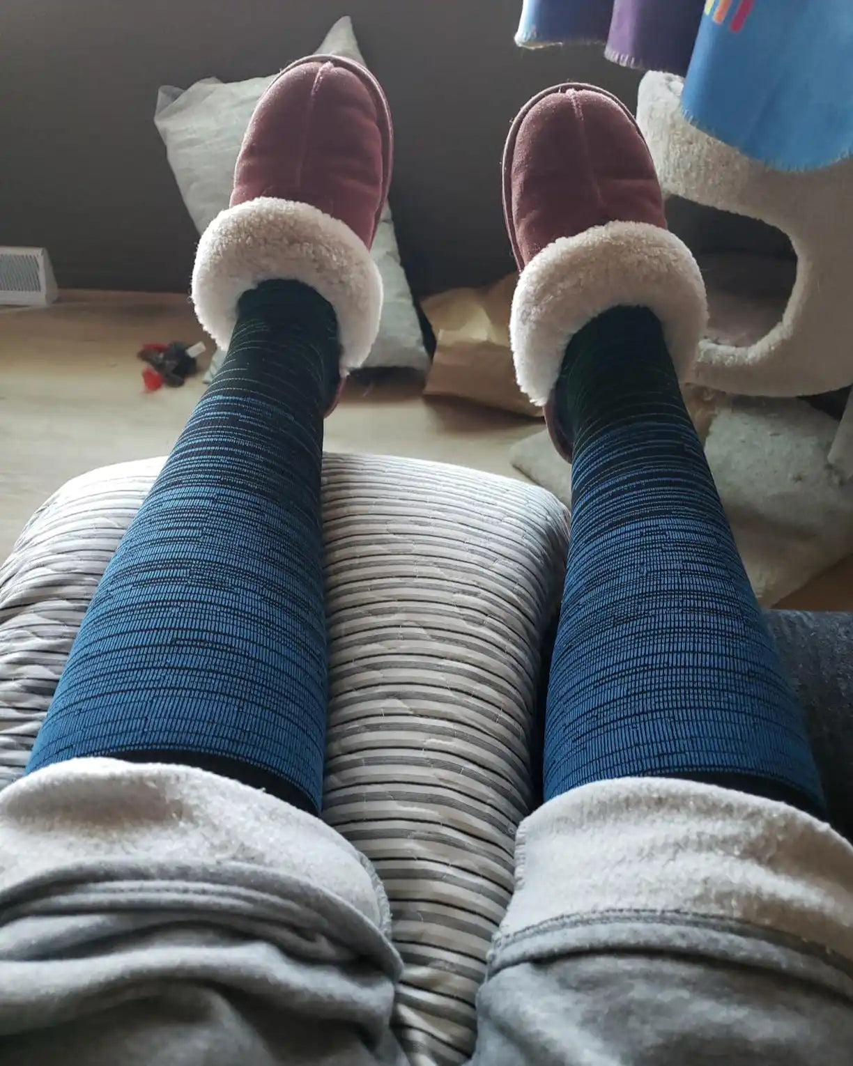 Jambes ornées de leggings côtelés douillets, bleu foncé, et de chaussons en velours bordeaux avec une bordure en fausse fourrure de couleur crème.