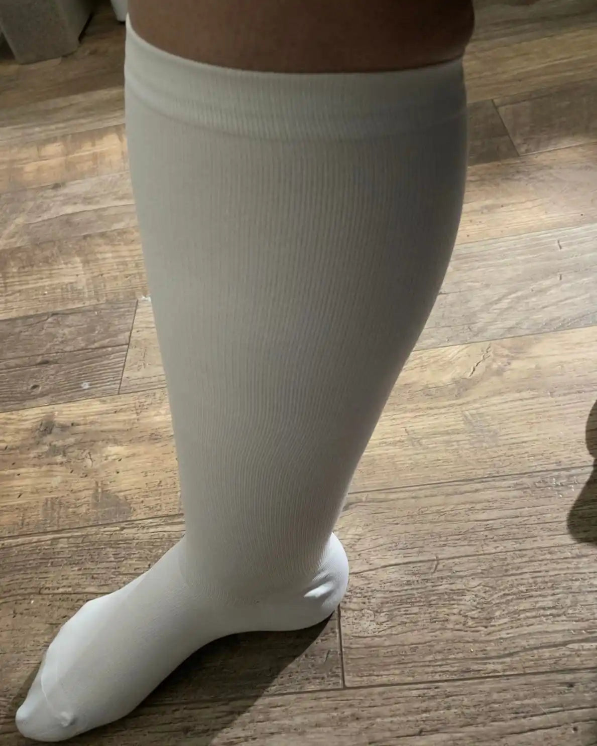 Une seule chaussette de compression blanche couvrant une jambe inférieure et un pied.